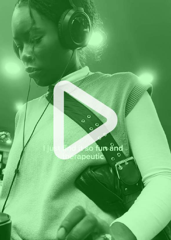 A girl wearing headphones spinning some vinyl in a record shop. The image is a still from a video with a play button overlayed