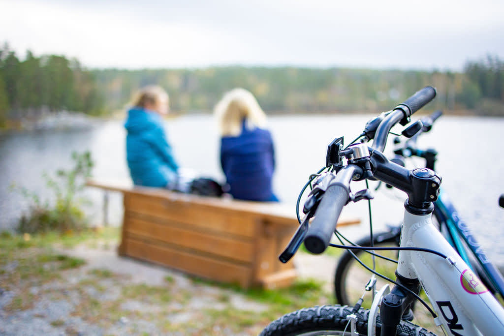 To jenter sitter på en krakk og ser ut mot havet. Syklene deres står i forgrunnen, og er i fokus.