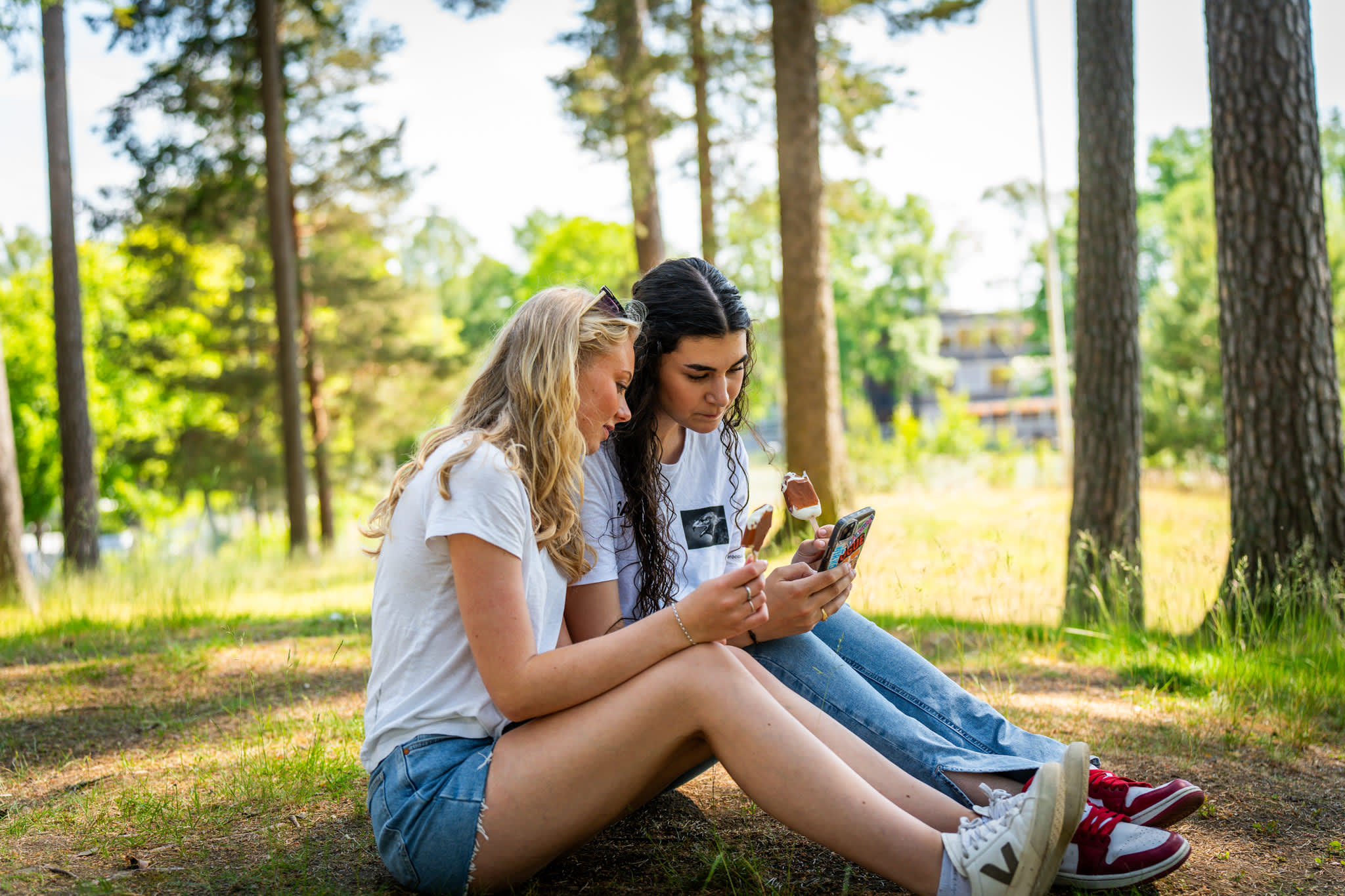 To jenter som sitter i parken og ser på telefonen til hverandre