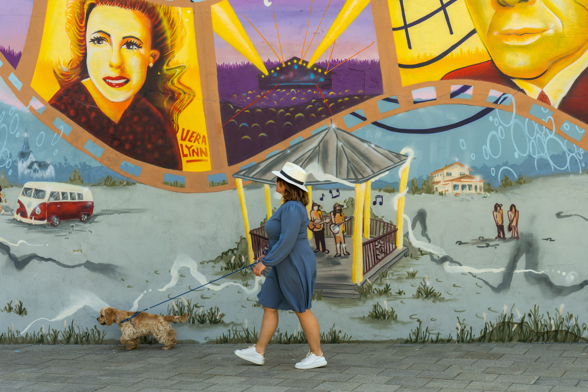 Dame med hund går forbi ett av veggmaleriene i Mysen