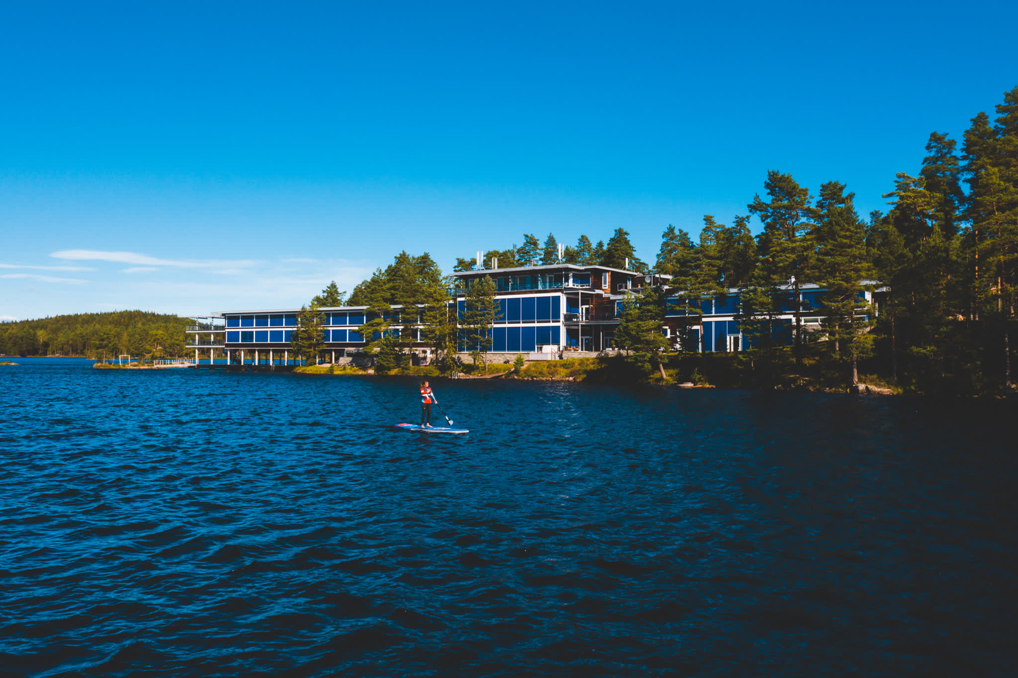 Image of the facade of the Rømskog spa hotel with a person on a SUP board on the lake in front of the building.