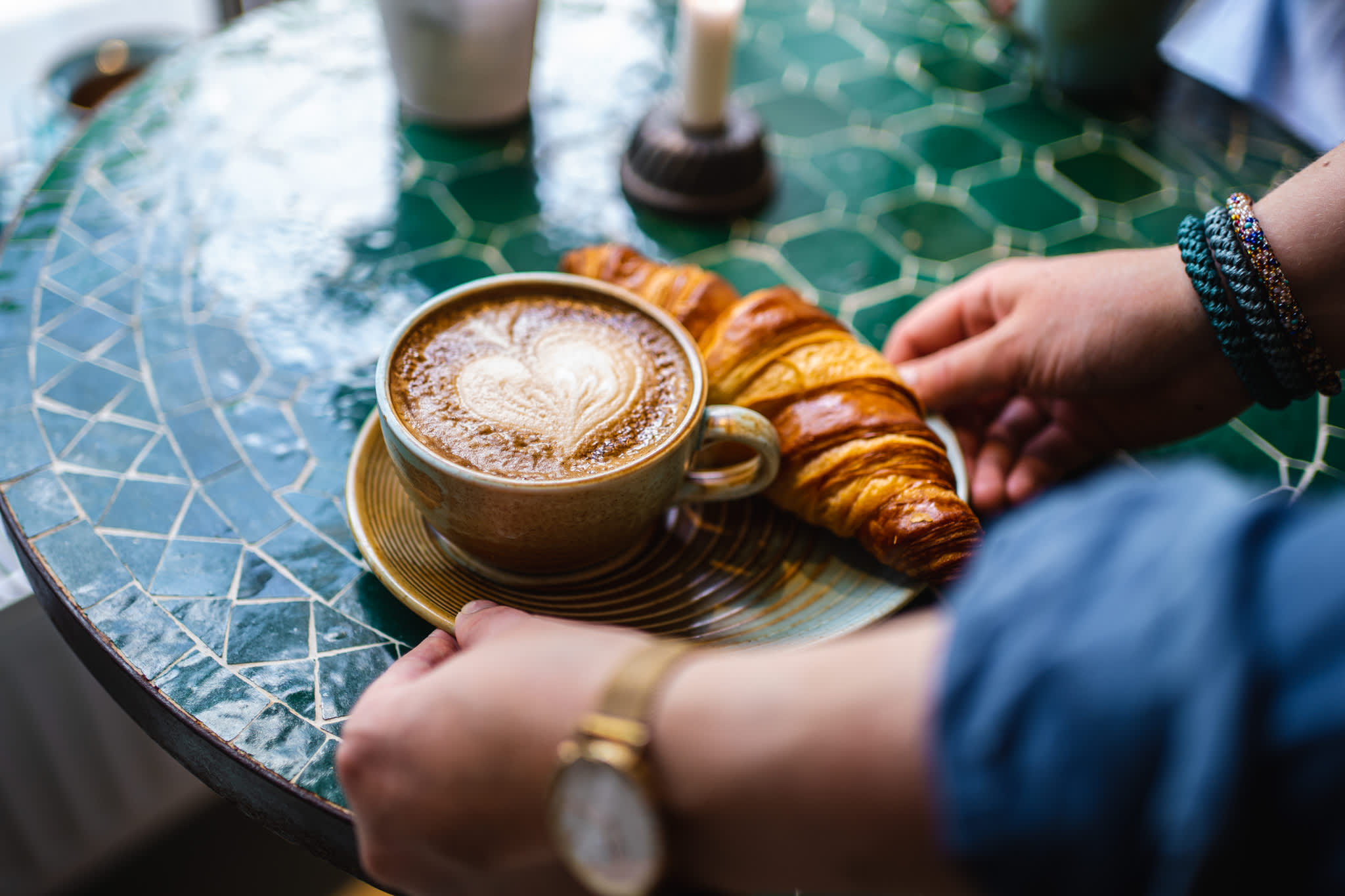 Kaffekopp med hjerteskum og en croissant servert på ett bord