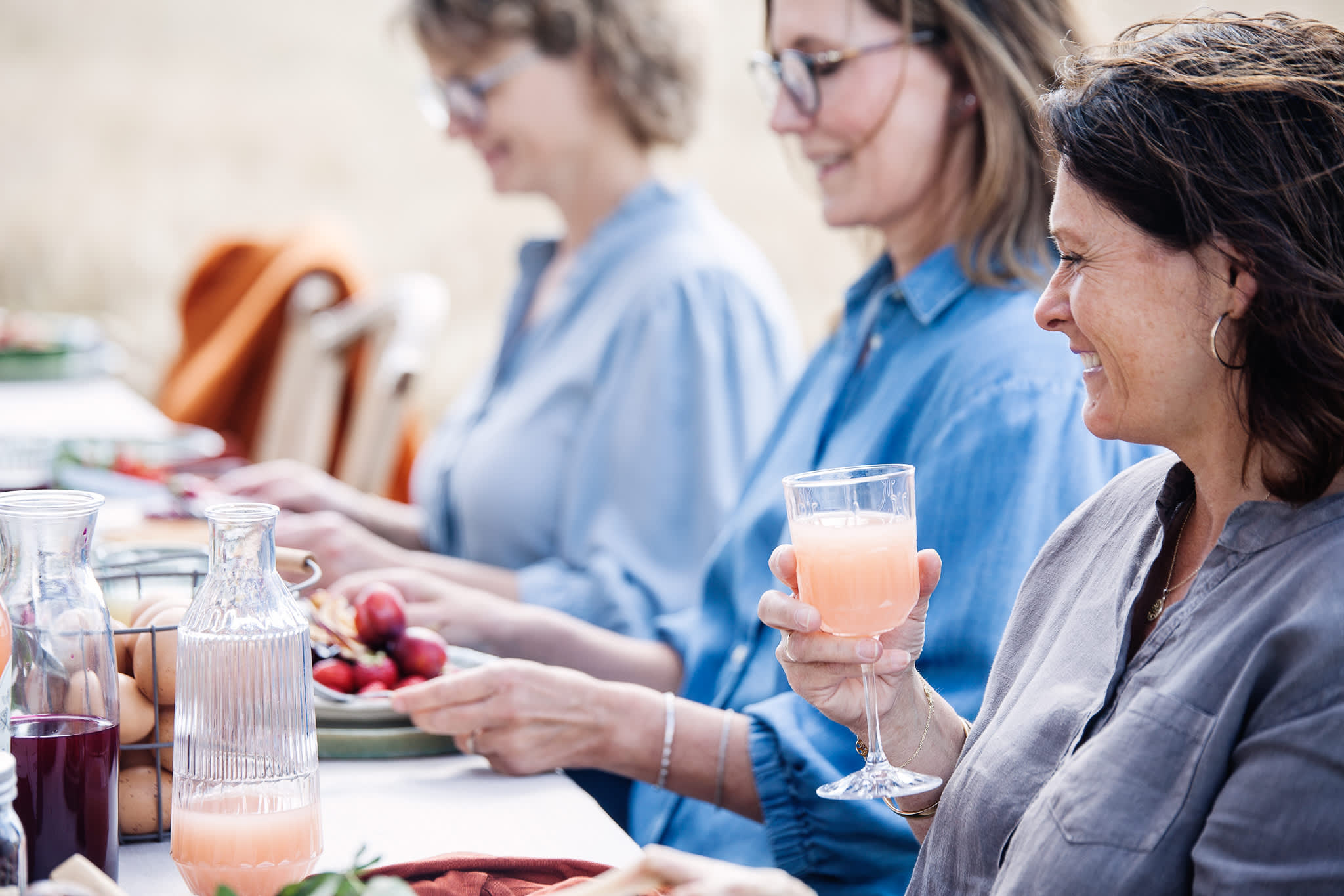 Tre damer spiser og drikker mat ved et bord utendørs