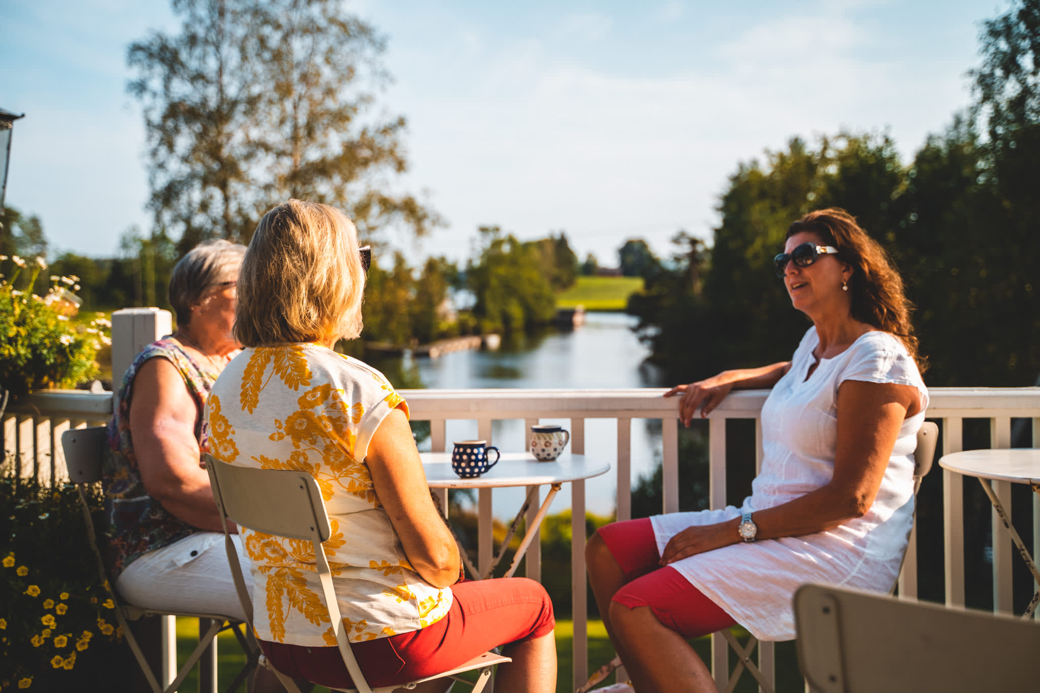 Tre damer nyter en kaffepause i kveldssola i Strømsfossen, Aremark