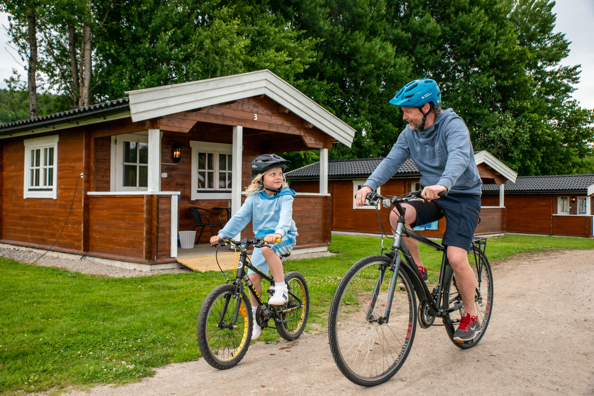 En mann og en jente på sykkel foran en camping hytte.