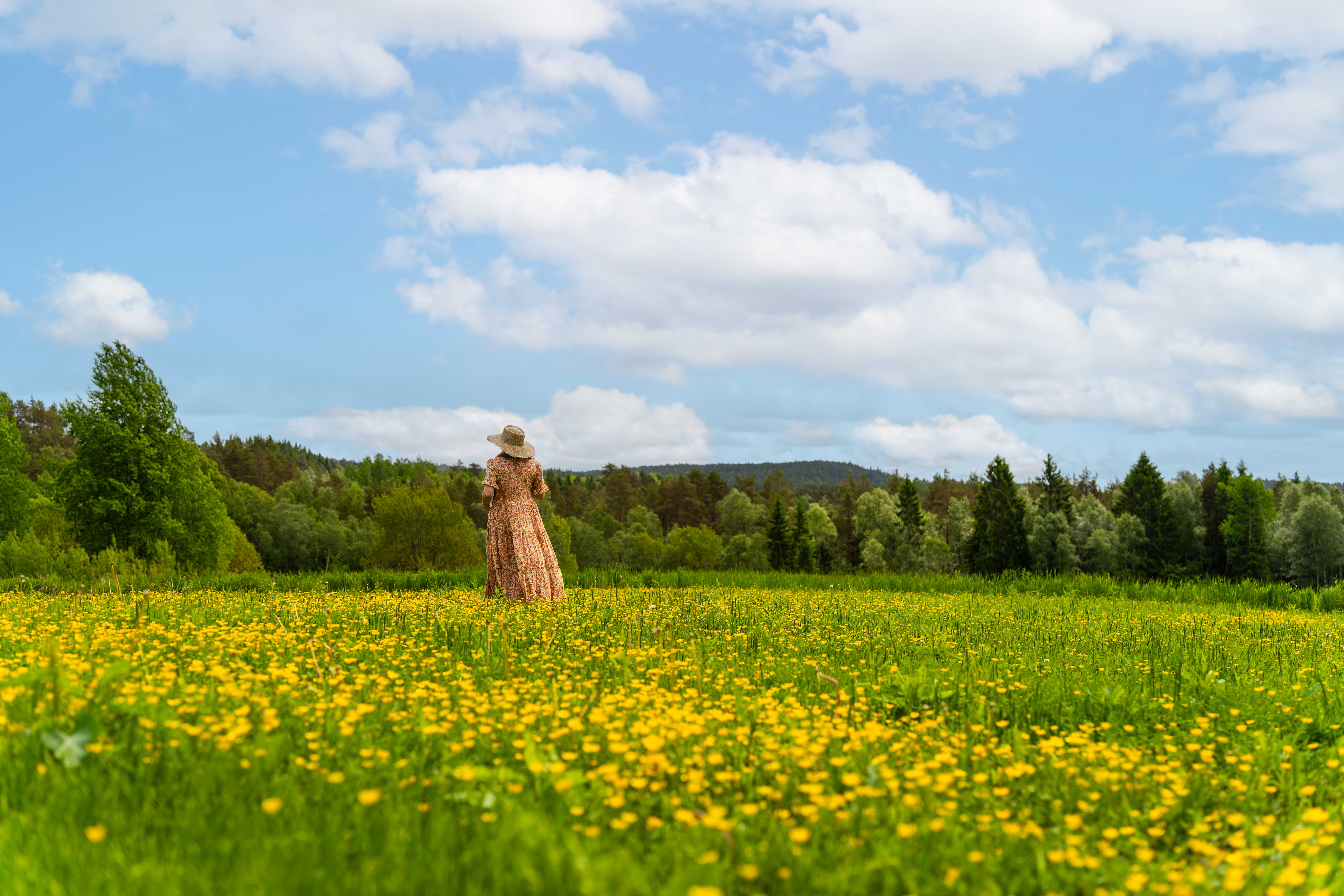 Kvinne i kjole som står i en blomstrende sommereng.
