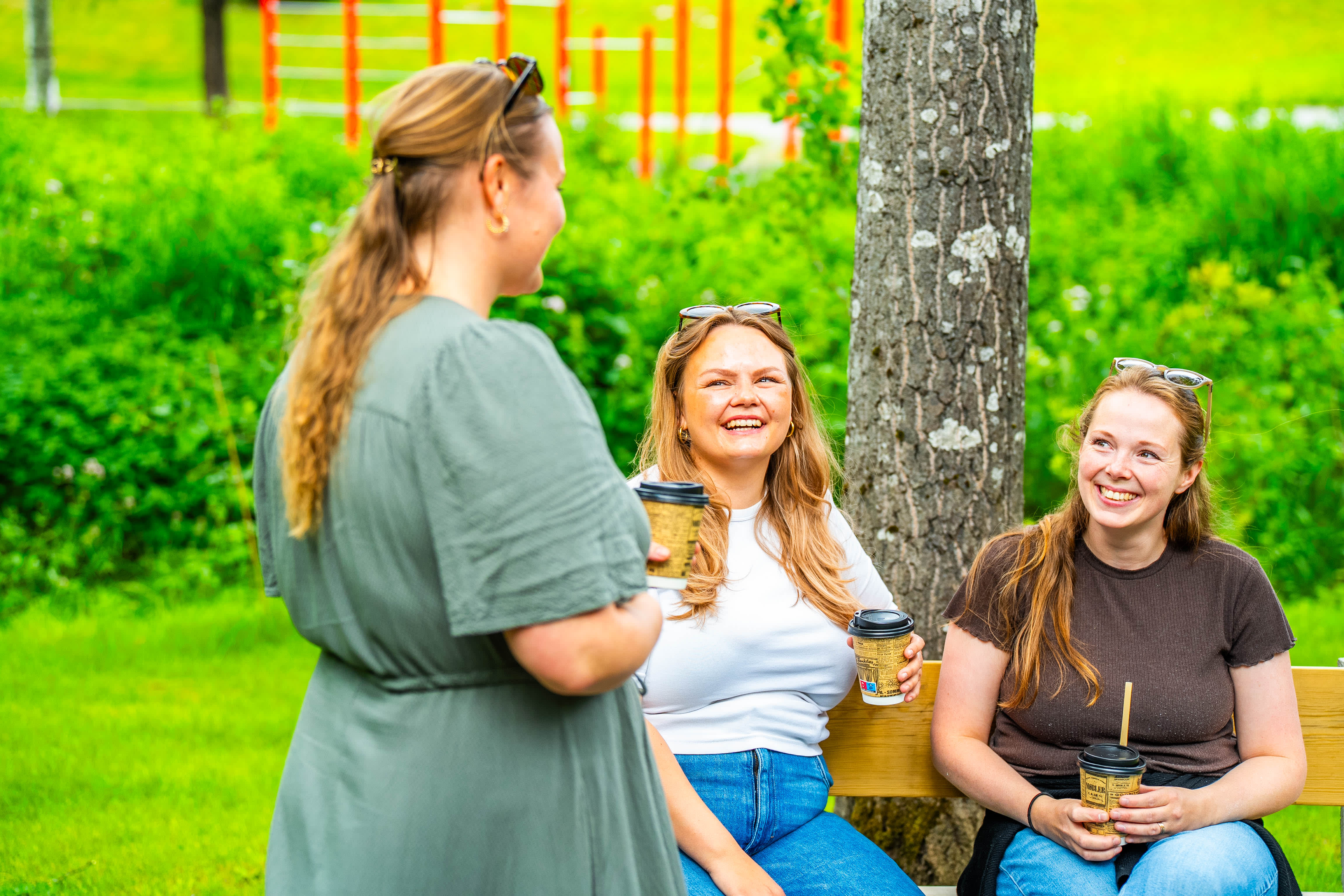 Tre jenter som drikkerkaffe og koser seg på tur i parken