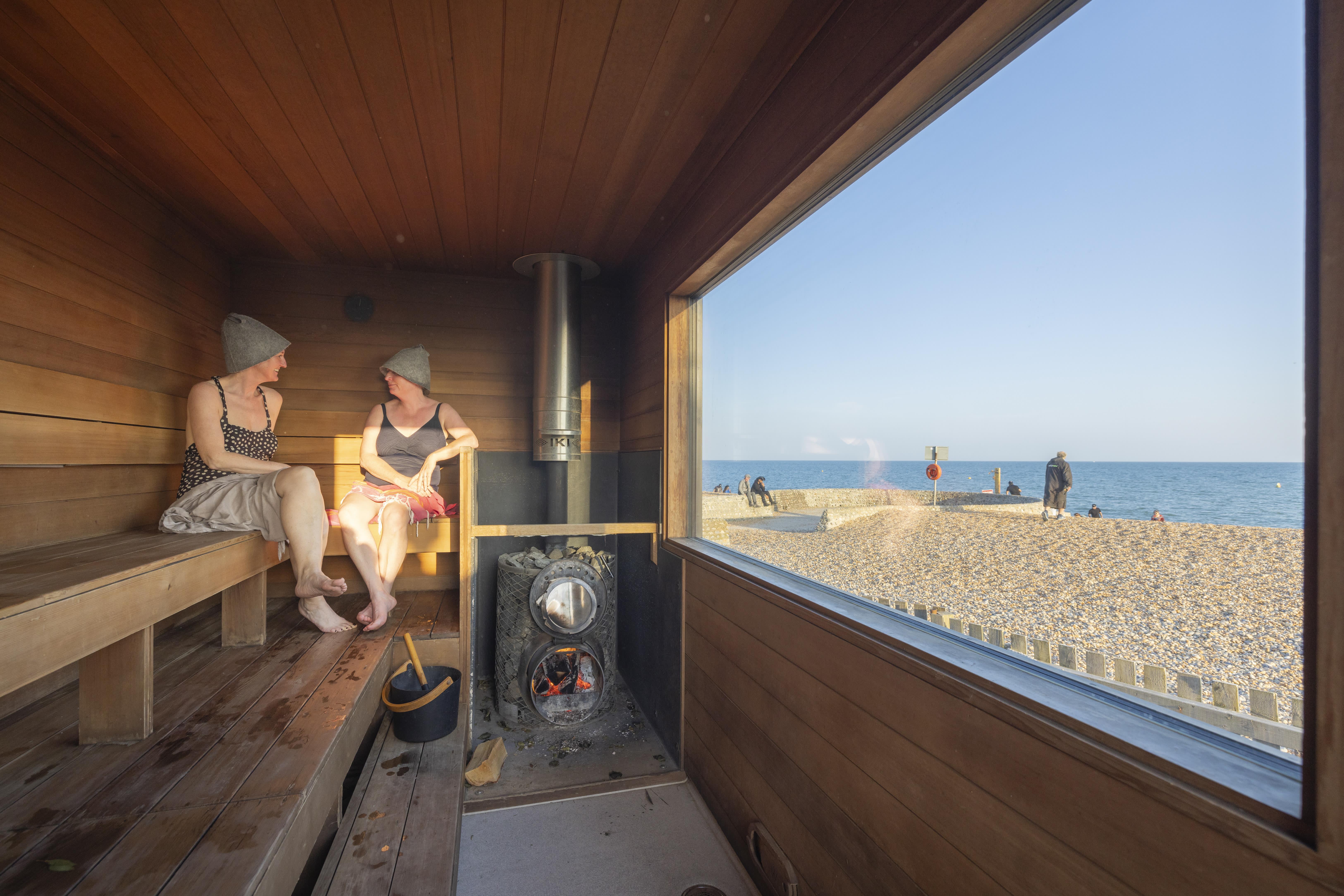 Two people sit in sauna on Brighton beach with view out to the sea