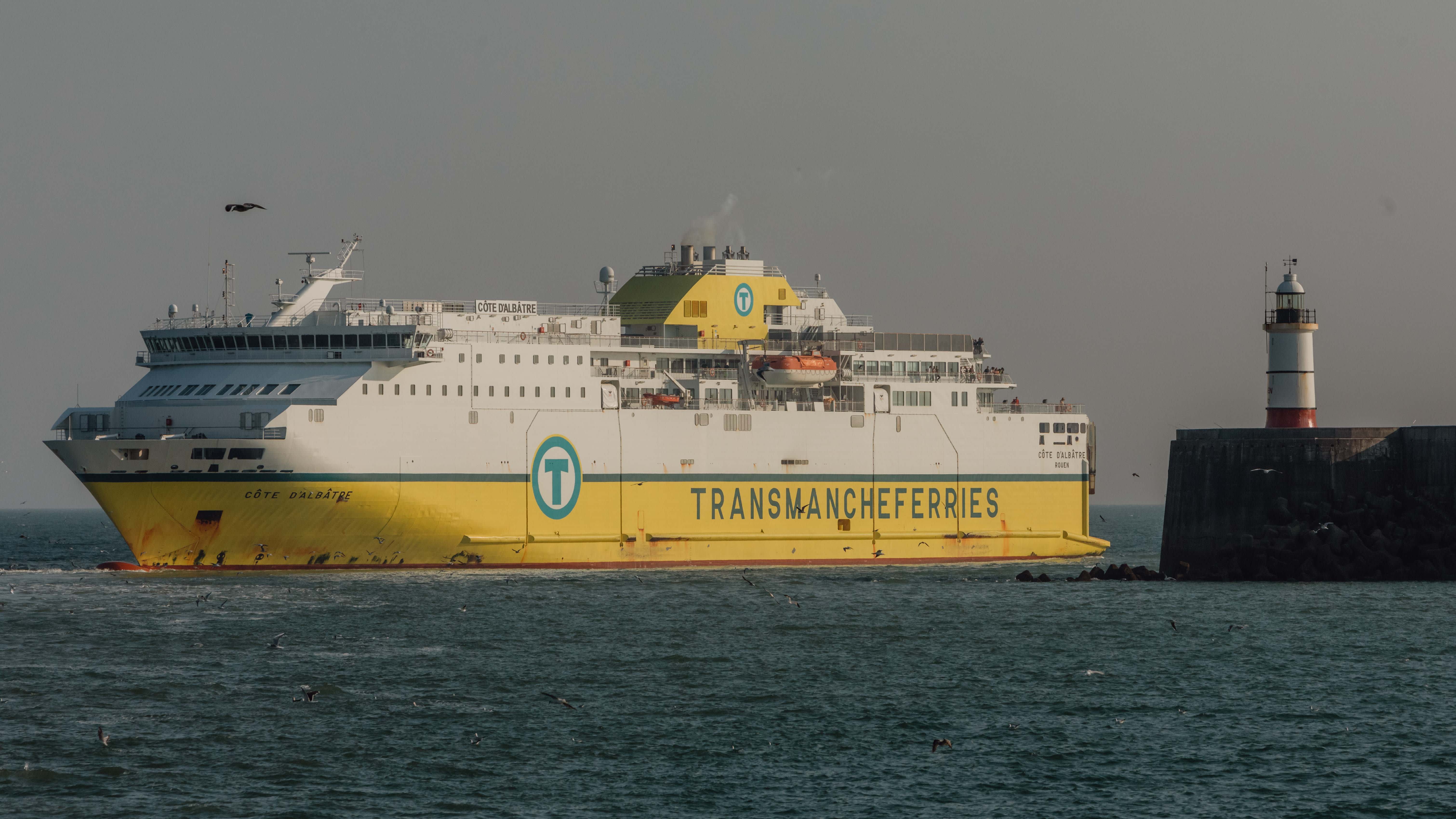 Yellow and white cross channel ferry coming in to port at Newhaven, with lighthouse in view