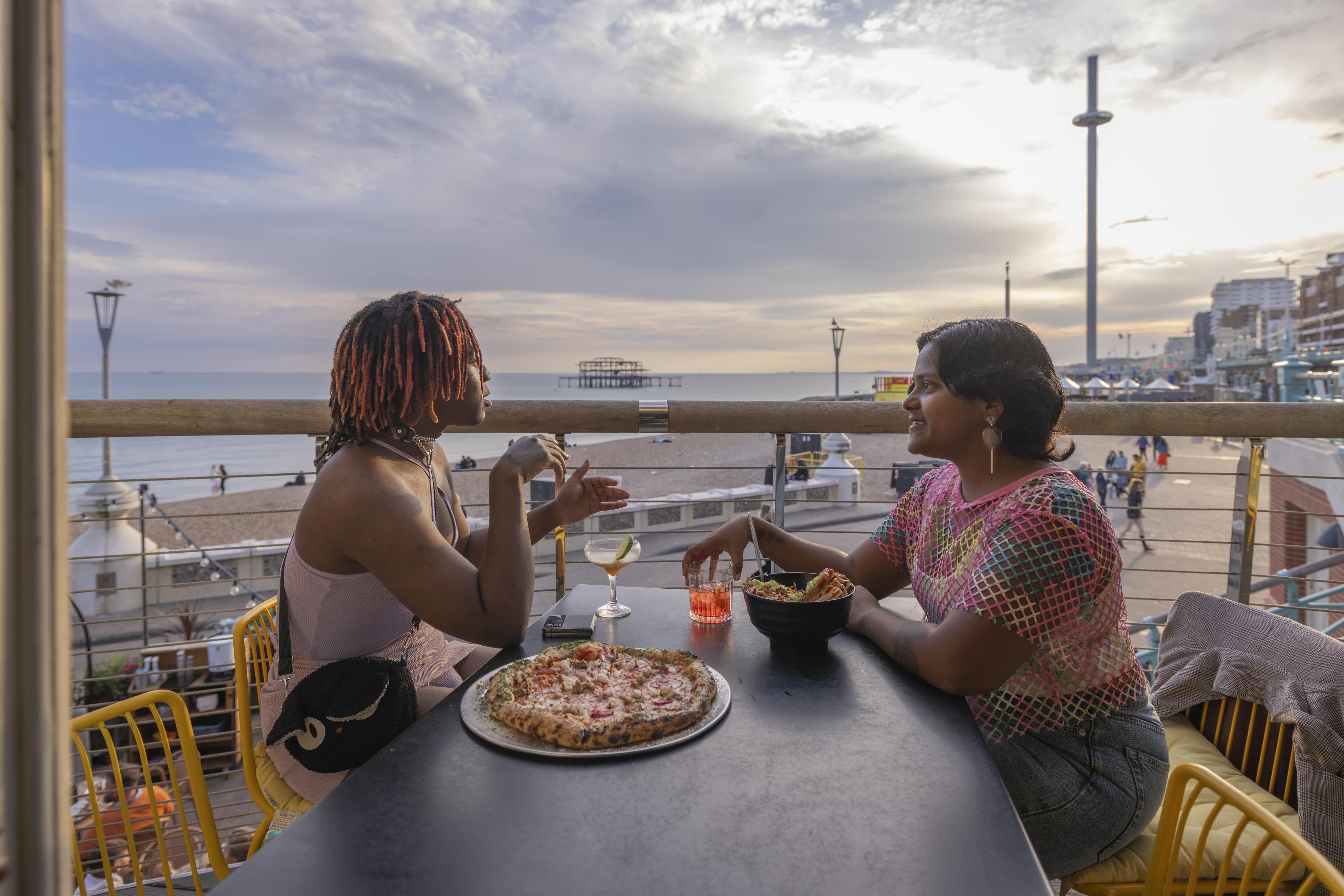 A couple eating and drinking at Shelter Hall in Brighton, with views to the sea