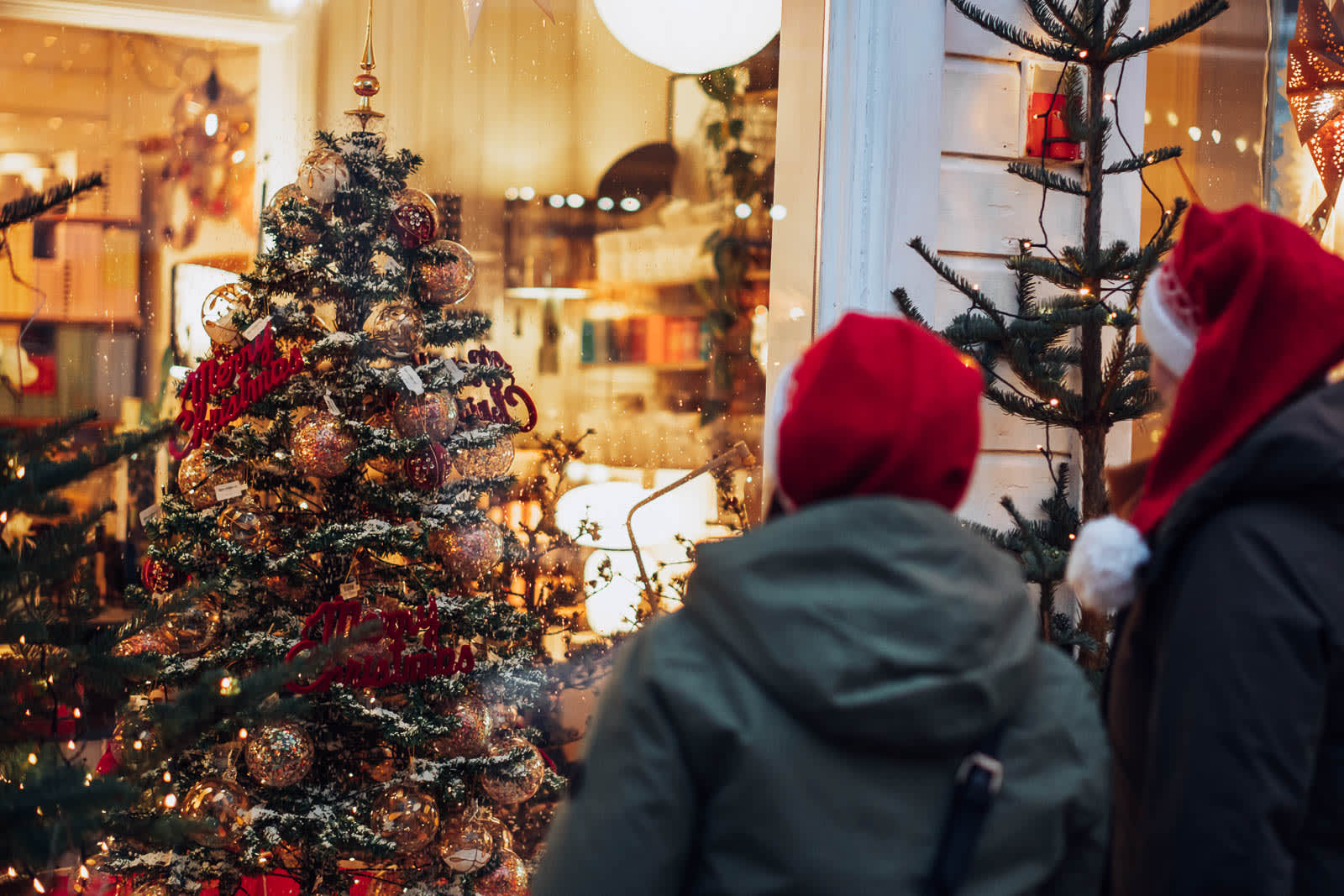 To personer med nisseluer ser på julepyntet butikkvindu