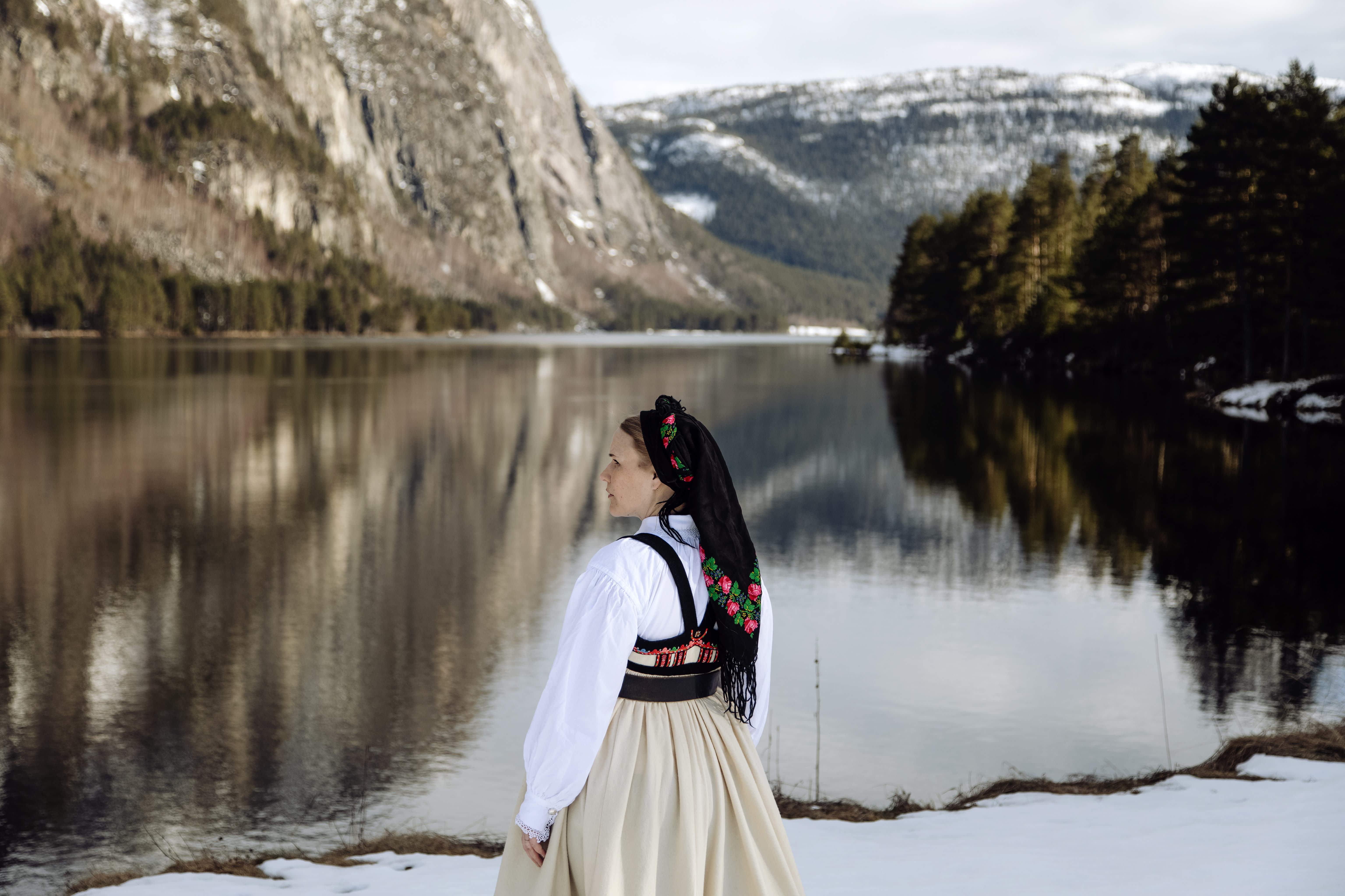 Young lady wearing national costume standing by the river and steep mountains. Photo