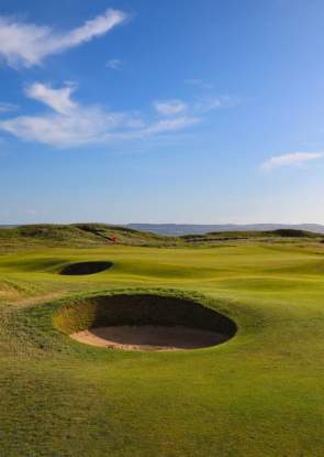 A bunker on a lush green golf course with blue skies