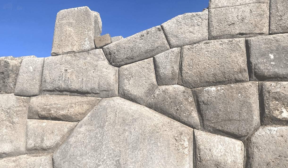 A wall made from mismatched, grey cement blocks against a blue sky