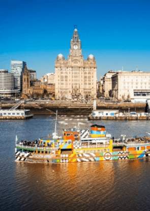 A colourful and patterned ferry on the Mersey River in the sunshine with the Royal Liver Building in the background