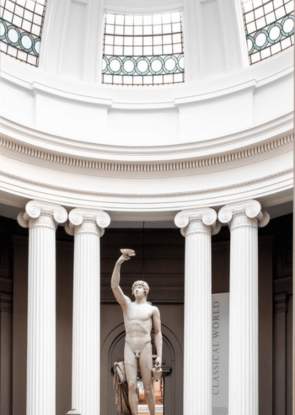 A sculpture of a male in a domed, Grecian style building with natural light pouring in