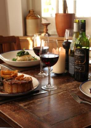 Two pub meals on a table next to two glasses of red wine