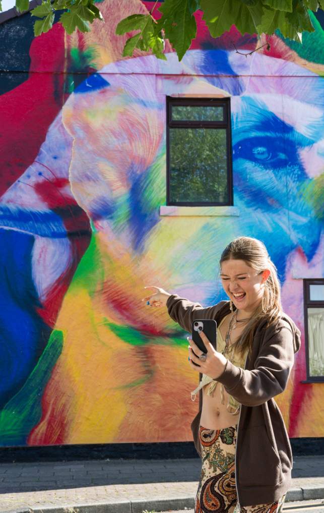 A girl takes a selfie in front of vibrant street art in New Brighton