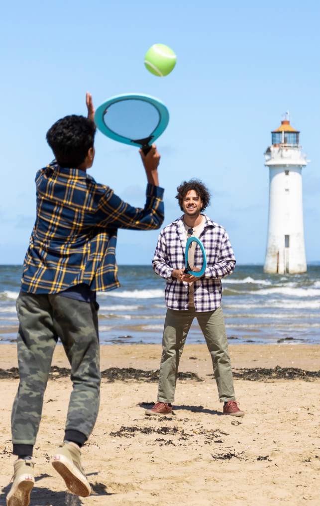 People play tennis on the beach in front of New Brighton Lighthouse