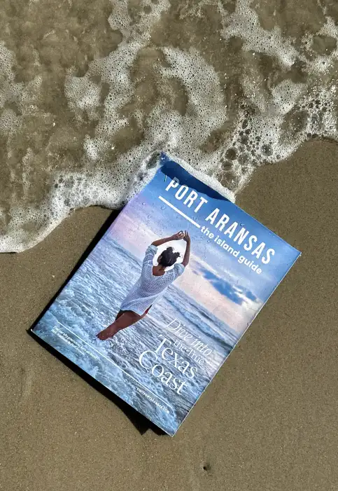 The island guide book in the sand with a wave going over top.