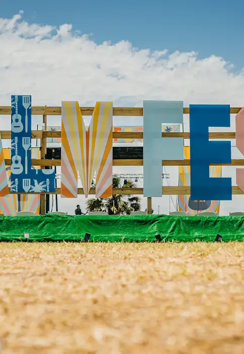 Up close shot of a large sign in the style of the Hollywood sign that reads "PalmFest." Each letter is painted in a different coastal pattern or color.