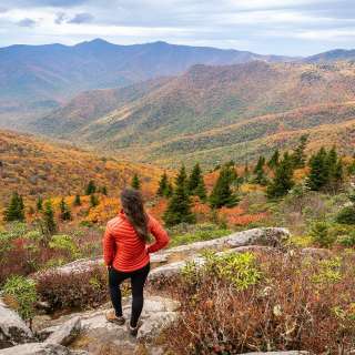 Woman wearing red jacket standing on top of mountain overlooking fall colors