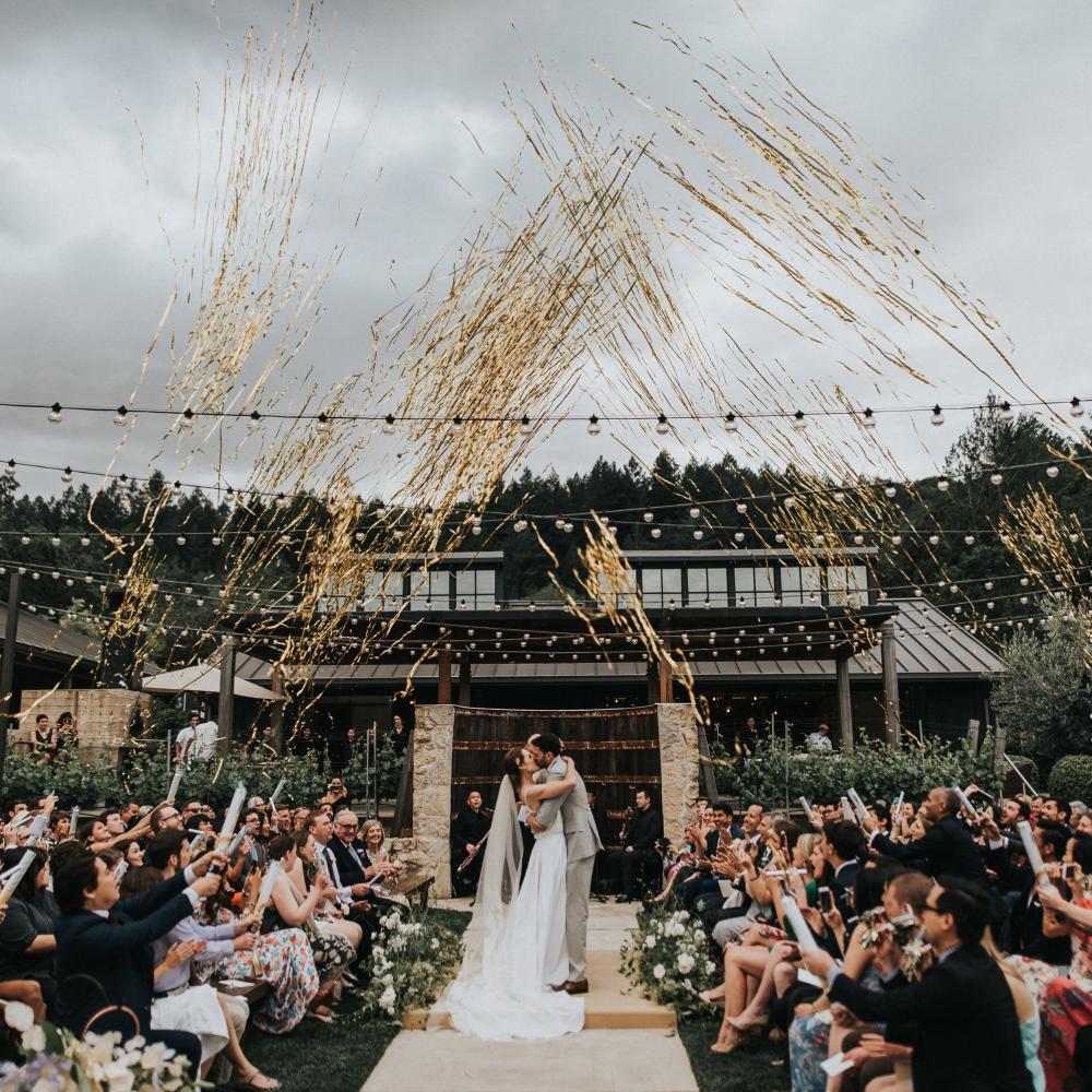 Bride and Groom kissing at the alter with guests shooting gold streamers in the air