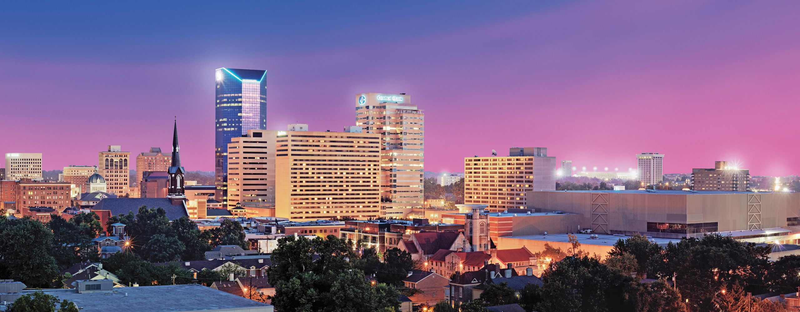 Lexington city skyline lit up for nighttime as the sun sets. The sky is blue and pink.
