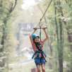 young smiling girl on zipline sails through muskegon state park forest