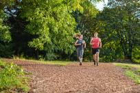 A couple runs on a bark mulch trail in a forested area.