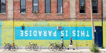 People walk by a wall mural that reads "This is Paradise" in Toronto's Queen Street West neighbourhood