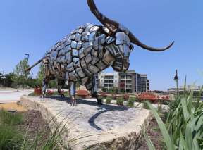 A large bull made from shiny chrome bumper guards stands on a rock slab in Wichita, KS