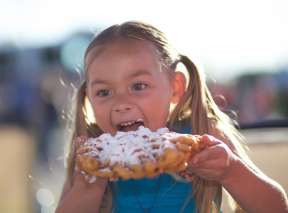 Little girl with pigtails eating funnel cake at Wichita Riverfest in downtown Wichita