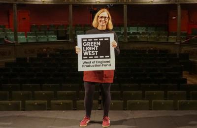 Mayor Helen Godwin on stage at Bristol Old Vic holding a sign that says Green Light West