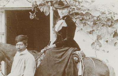 Black and white photo of a woman on a horse being led by a man