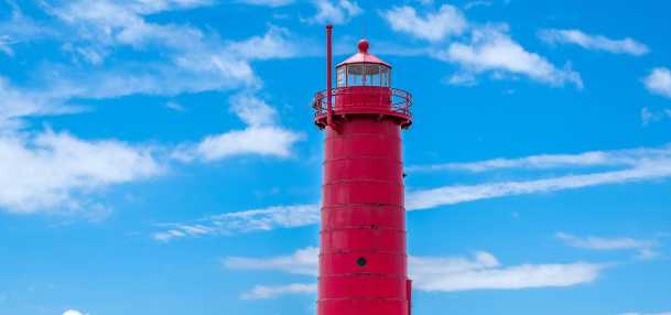 red historic lighttower at end of pier set against blue sky and clouds