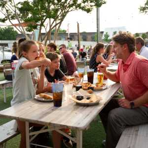 Family eating pizza and breadsticks on an outdoor picnic table at Parlour in Jeffersonville, IN