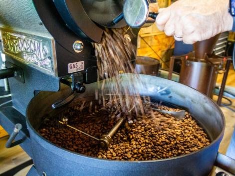 A hand can be seen holding a lever that releases freshly roasted coffee beans, which are pouring from the spout and collecting in the container below.