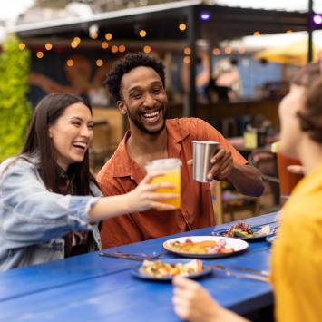 Two women and a man cheering drinks over plates of tacos.