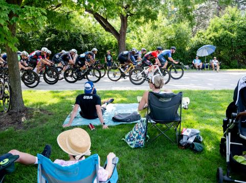 People sitting on grass watching professional bike race go by on street