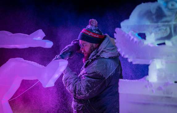 An ice sculptor using a power tool to carve a block of ice at the Freezefest ice battle