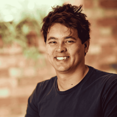 A headshot of Matt Pierri looking at a camera wearing a black t-shirt. They have brown hair and the background is a brick wall.