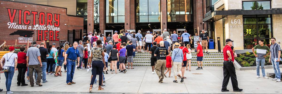Image of a crowd milling around Segra Stadium courtyard/entrance with mural "Victory Means a Little More Here"