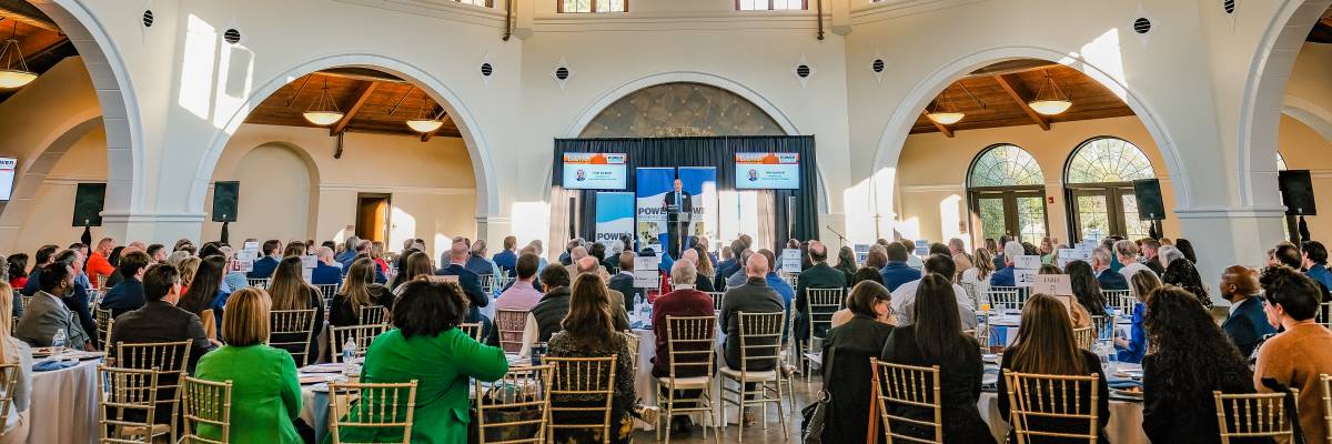 Conference attendees seated inside the Cape Fear Botanical Garden event hall in Fayetteville, NC, listening to a speaker under the vaulted wooden ceiling.