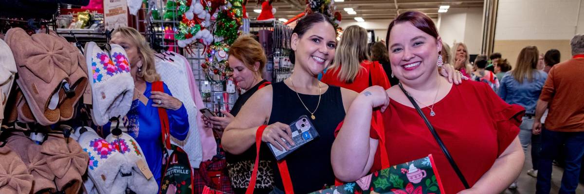 Shoppers smile and hold festive tote bags while browsing booths of holiday gifts and handmade crafts at the Holly Day Fair inside the Crown Expo Center in Fayetteville, NC.