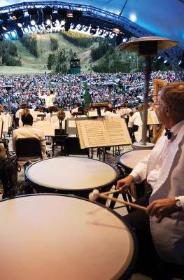 View of Symphony from backstage with timpani drum player in foreground and conductor and crowd in the background