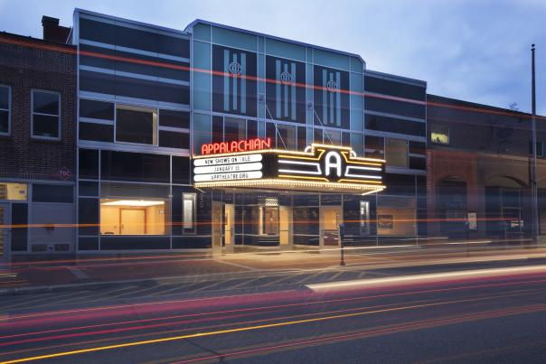 The facade of the Appalachian Theatre at dusk can be seen behind the artistic light trails left by car headlights on King Street. The theatre's marquee is glowing, announcing show tickets on sale now.