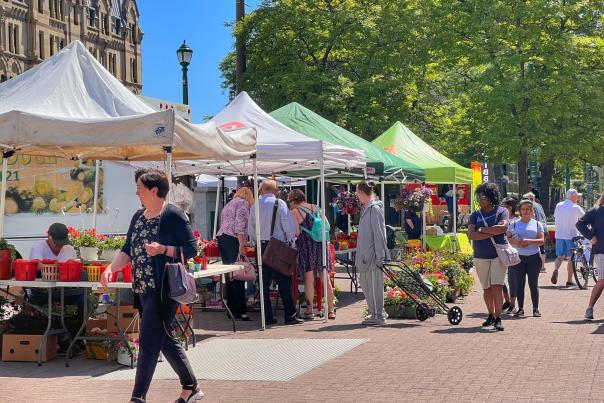 landscape photo of downtown Farmer's Market in Clinton Square. People are shopping and looking at fresh fruit and vegetables.