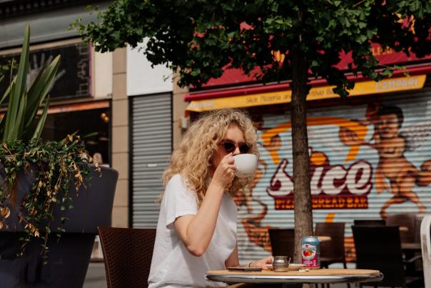 Person drinking coffee outdoors with sunglasses on