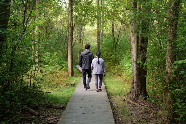 Couple walking on wooden boardwalk trail through lush green forest in Summit Metro Parks, Akron, OH.